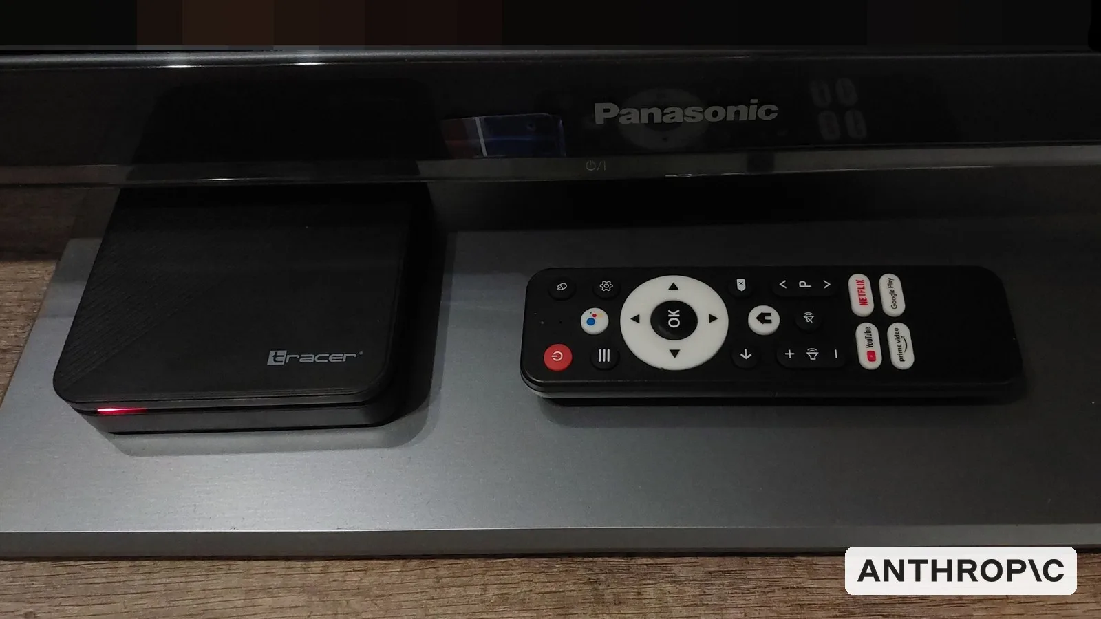 An Android TV set-top box and remote under a television, with the Anthropic logo